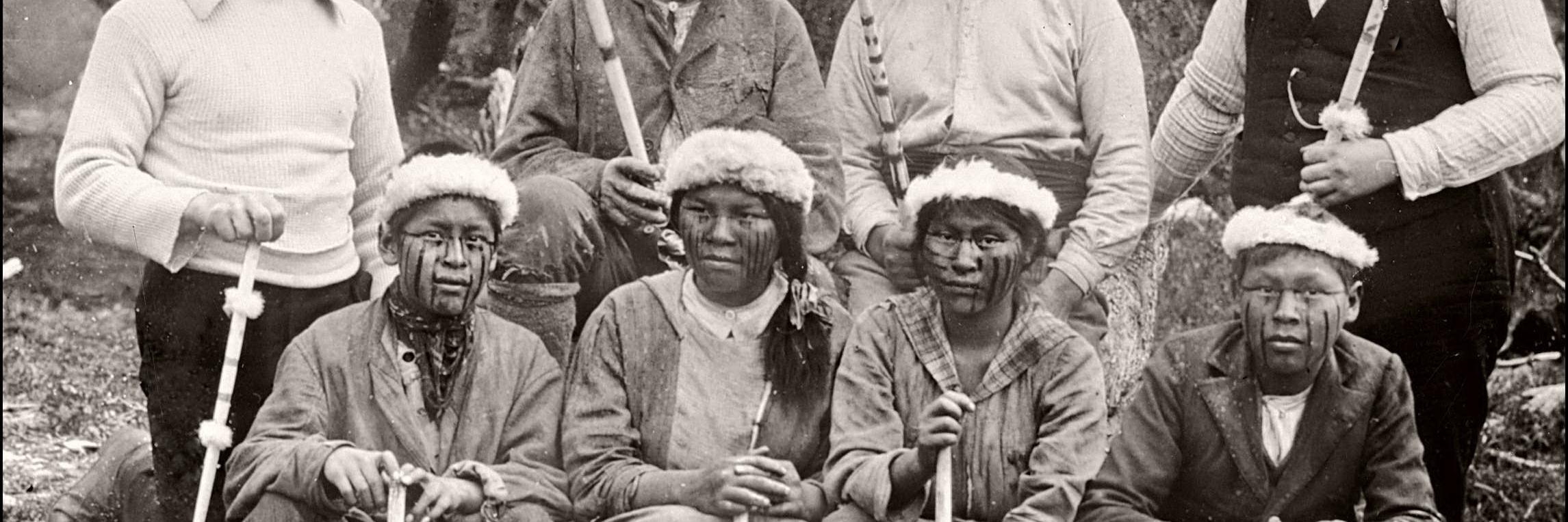 Martín Gusinde arriba a la izquierda y Wilhelm Koppers arriba a la derecha, junto a un grupo de Yámanas o yaganes (Publicada en Koppers 1924 y con copia en el Museo Histórico Nacional).